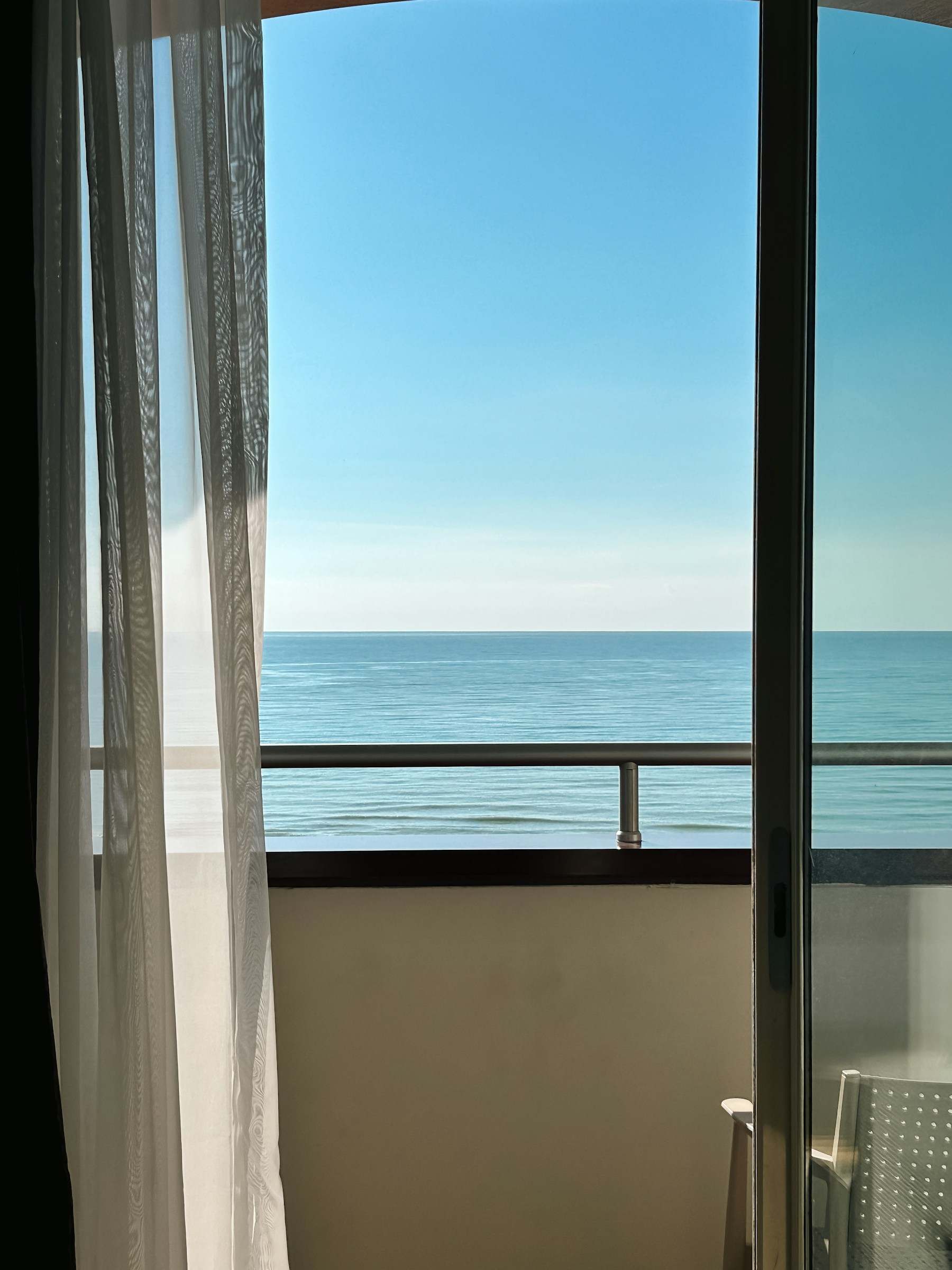 Varanda com porta de vidro aberta e guarda-corpo, de frente para o mar azul