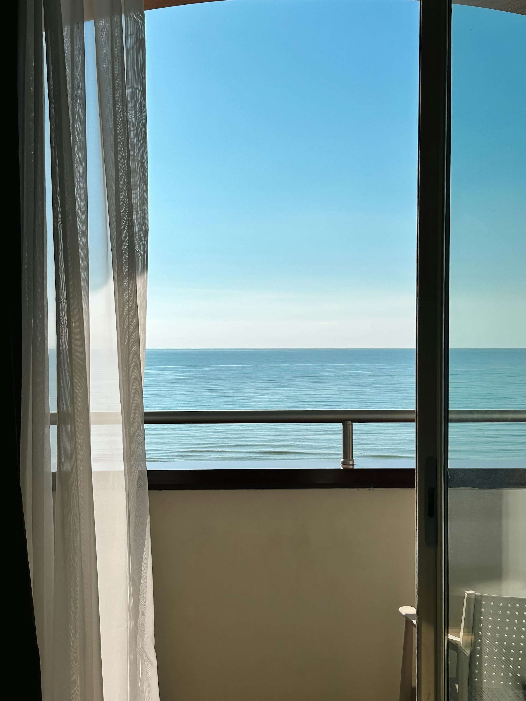 Varanda com porta de vidro aberta e guarda-corpo, de frente para o mar azul