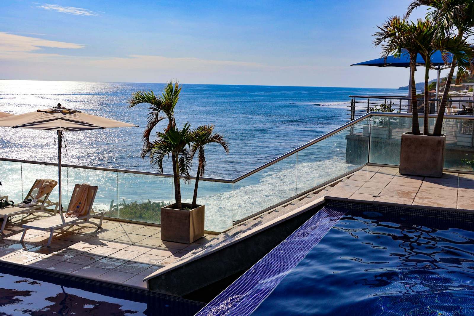 Terraço com piscina e guarda-corpo de vidro de frente para o mar, com palmeiras