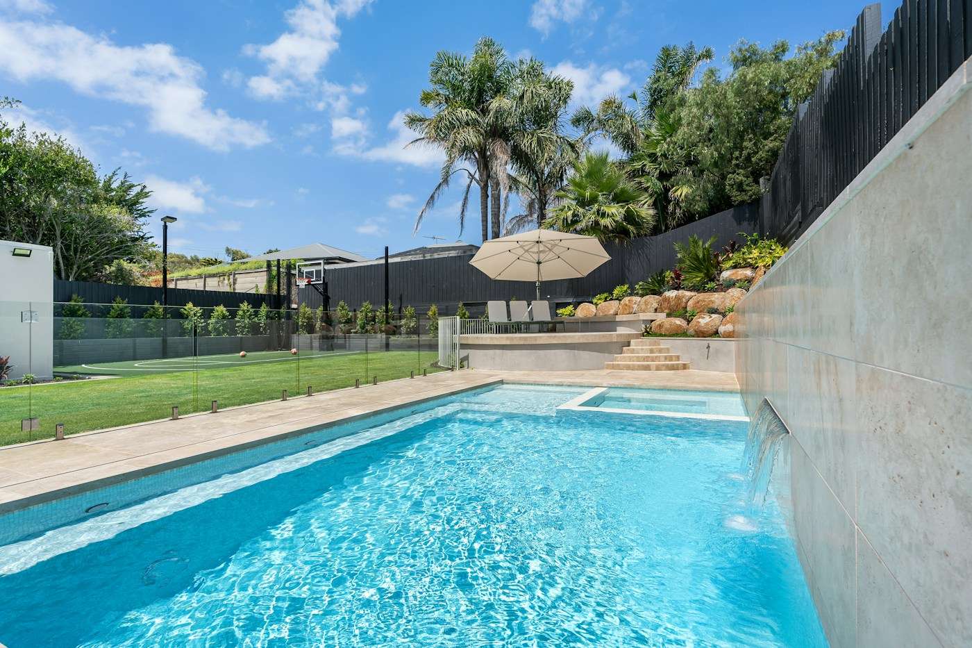 Piscina cercada por guarda-corpo de vidro, com palmeiras e jardim