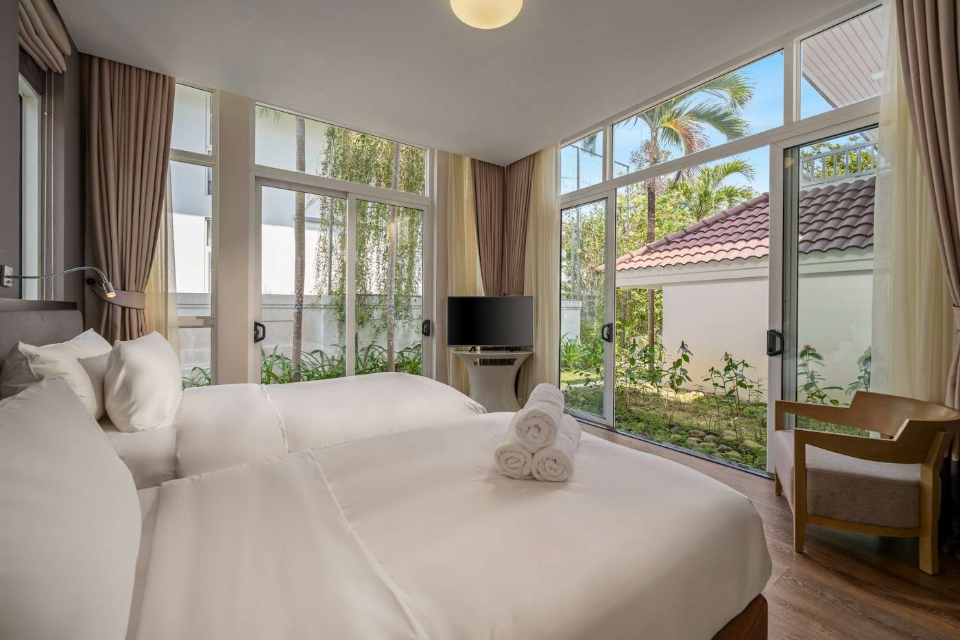 Quarto claro com janelões de vidro voltados para jardim tropical