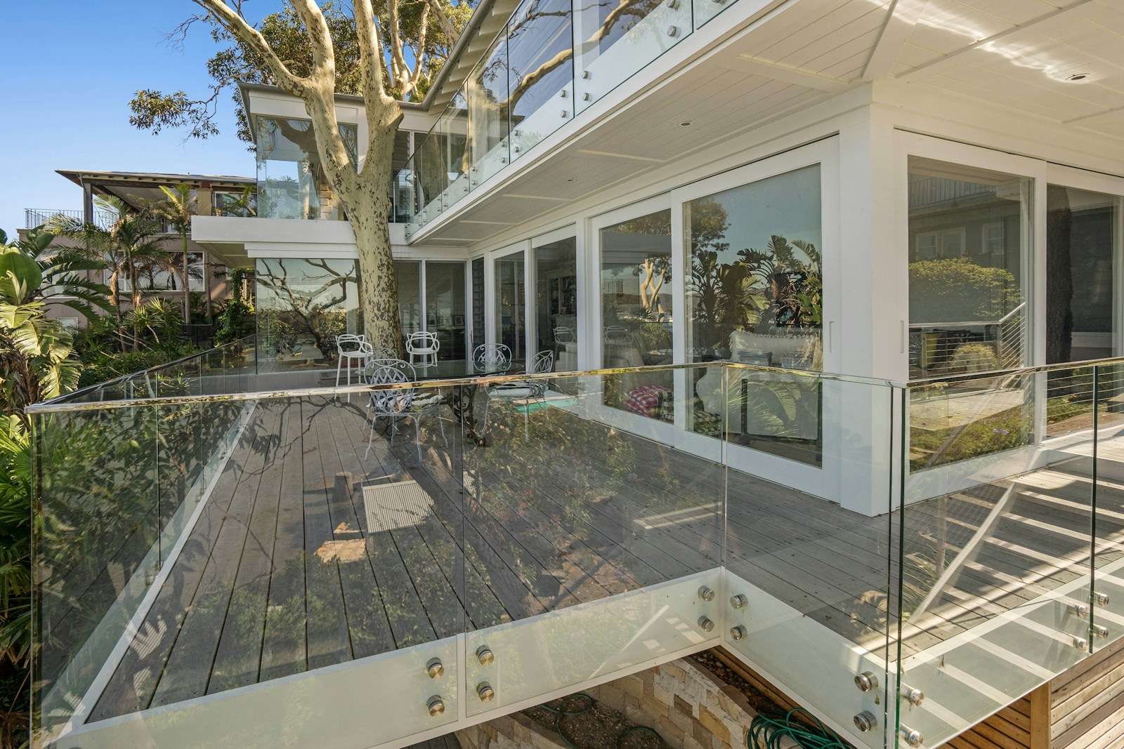 Casa com varandas fechadas por guarda-corpo de vidro, entre árvores